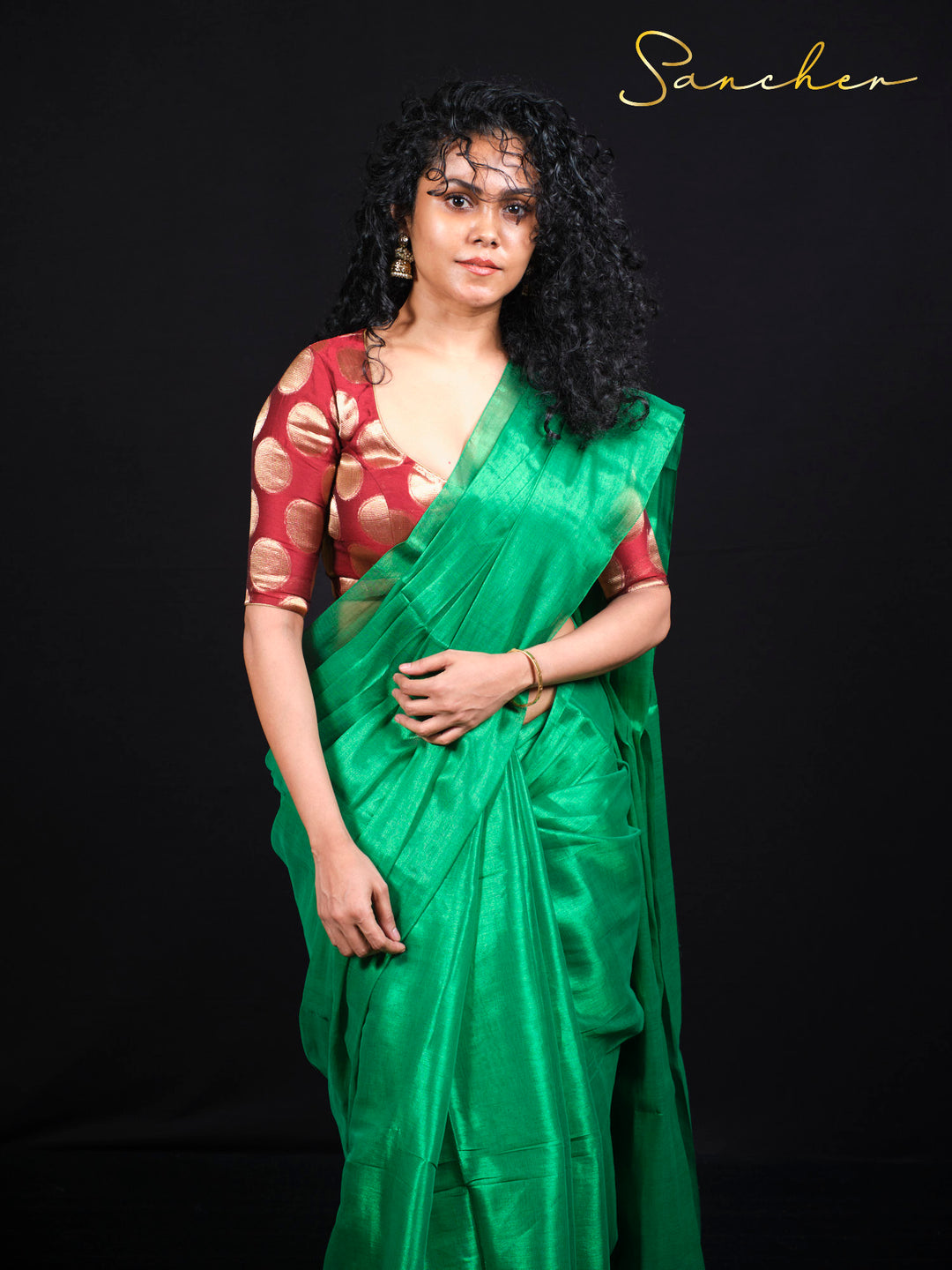 Standing pose of emerald green mul zari saree with golden polka dot blouse piece styling