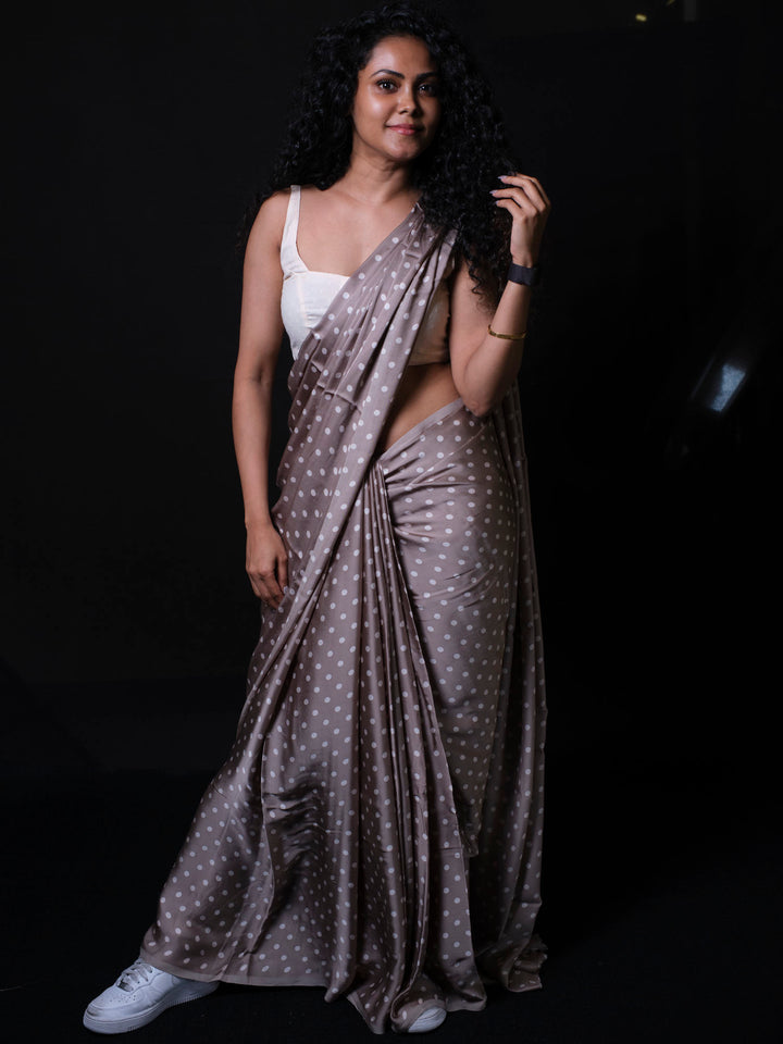 Woman wearing dusty taupe modal silk saree with white polka dots and white sneakers against dark background