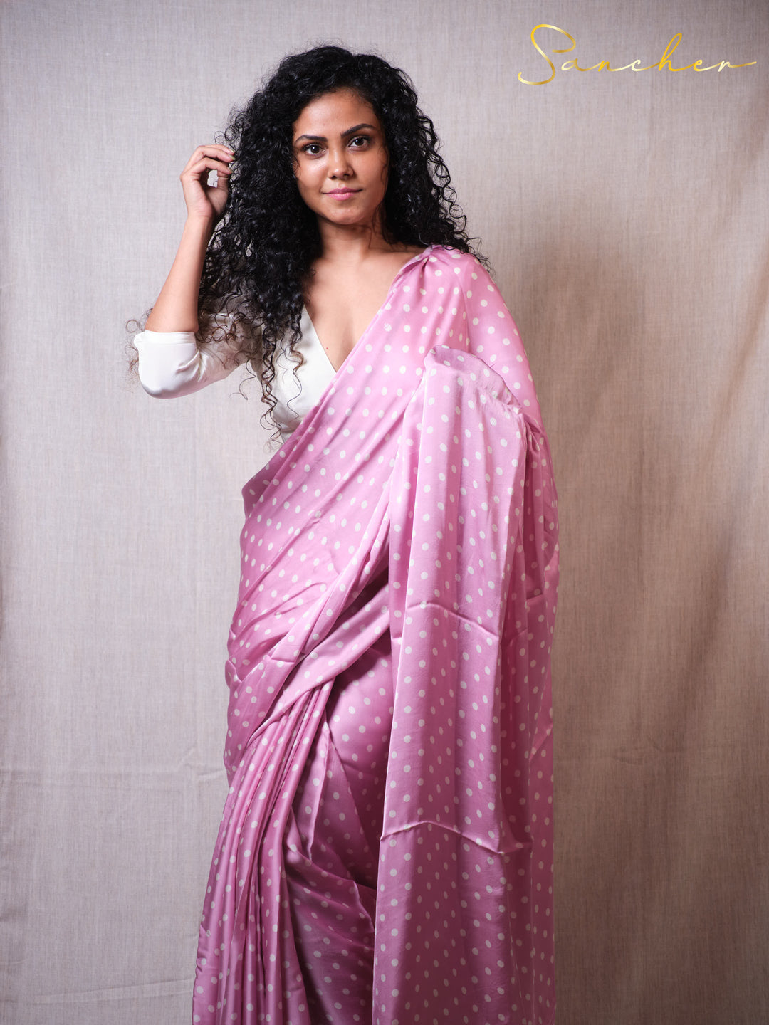 Woman wearing a pink saree with white polka dots against a plain background