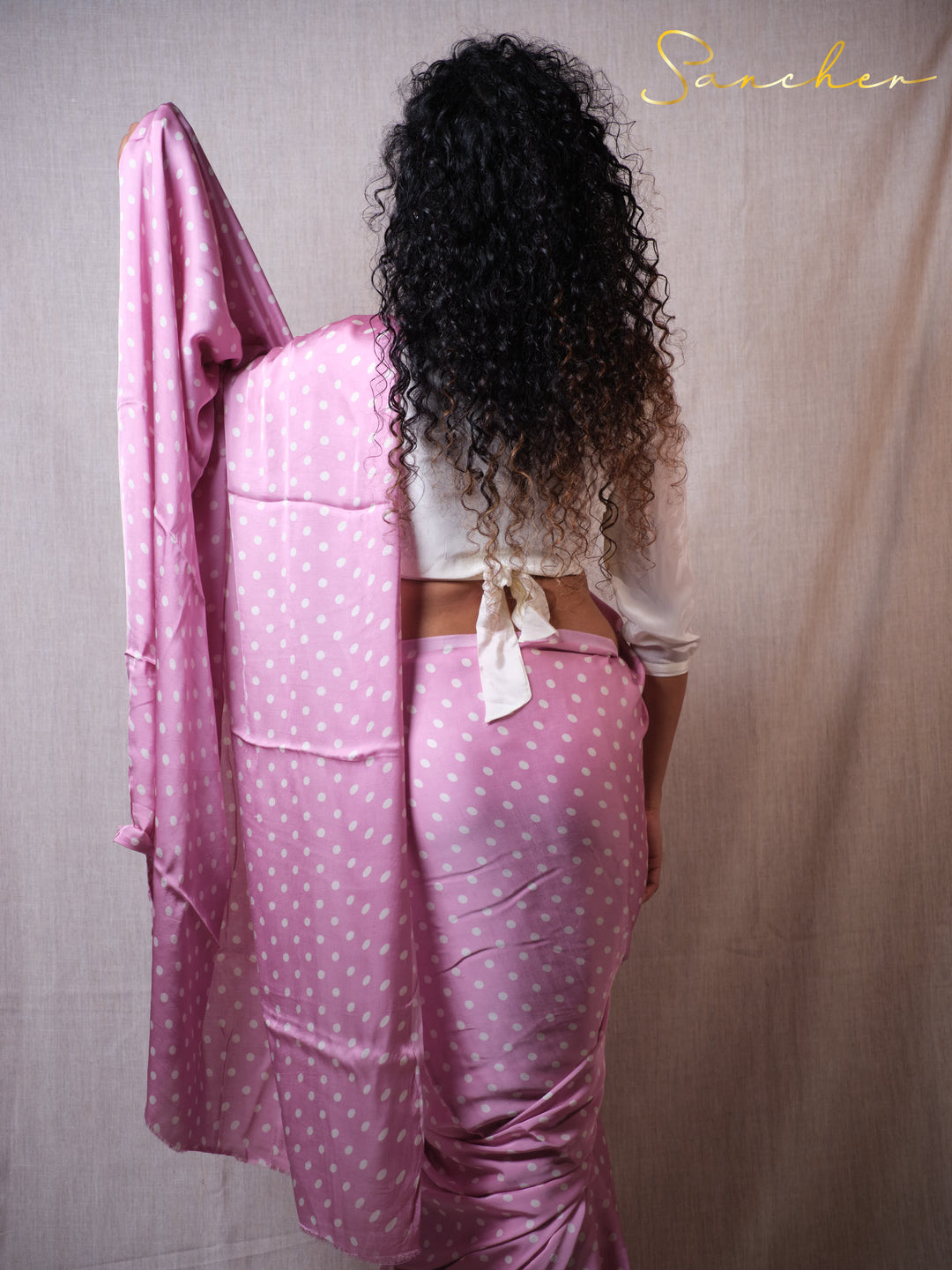 Sancher wearing a pink polka dot outfit with a white top, standing against a plain background.
