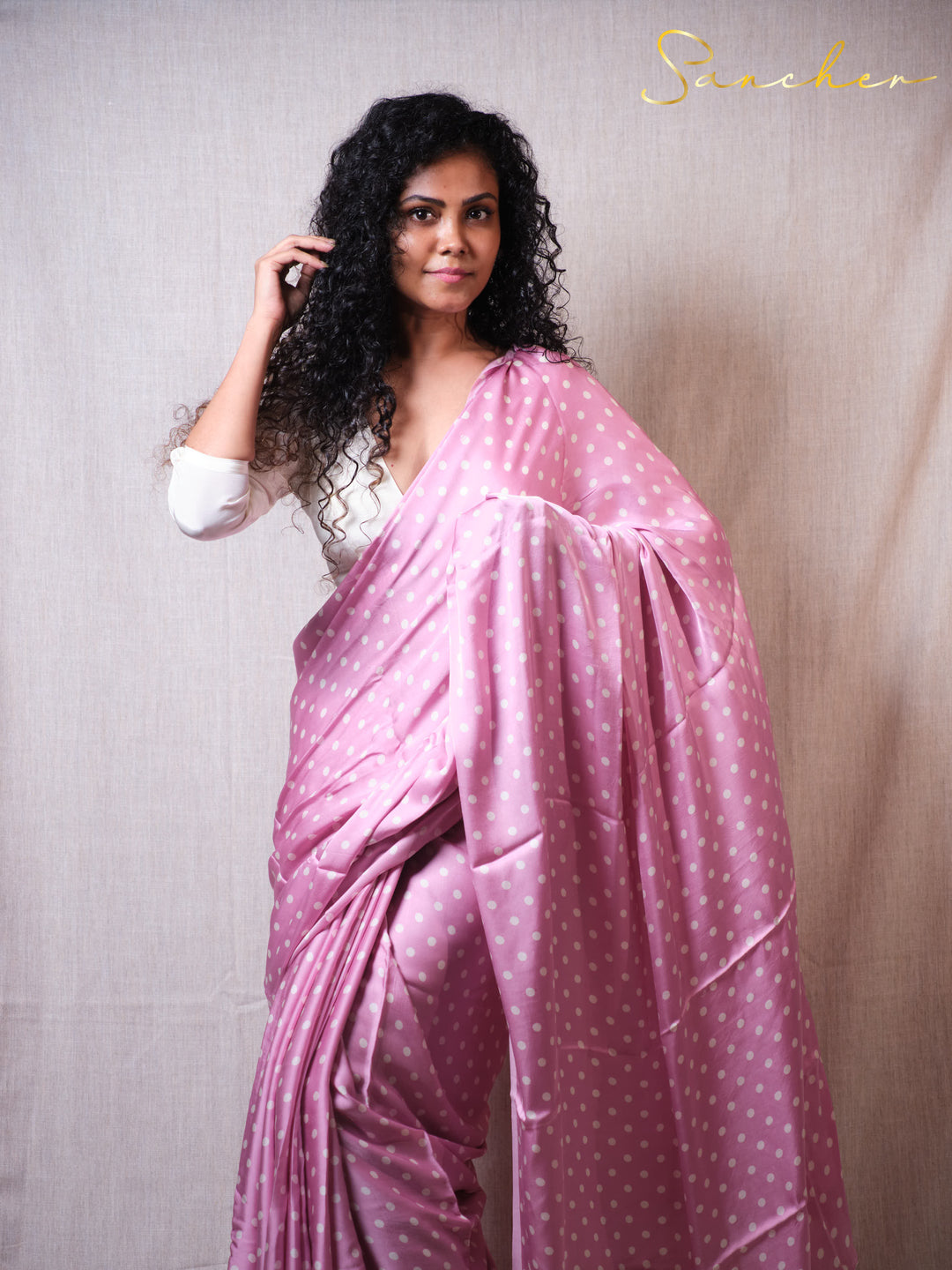 Woman wearing a pink saree with white polka dots against a plain background