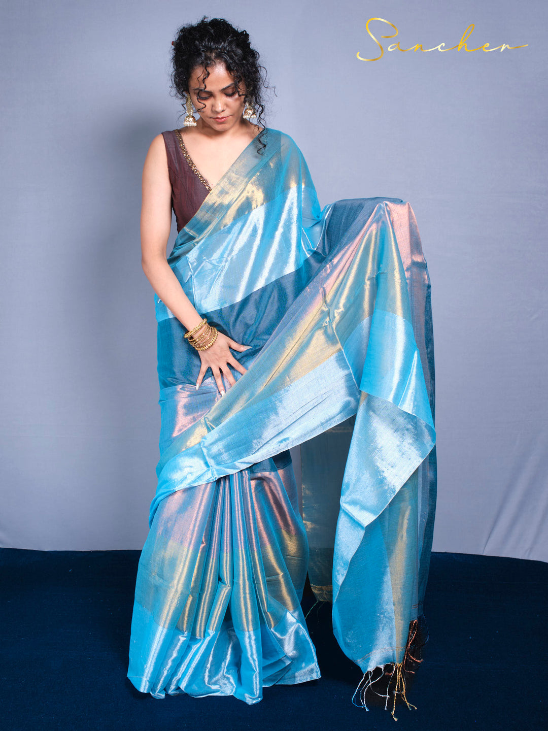 Elegant woman showcasing sea shine saree with curly hair and gold jewelry accessories