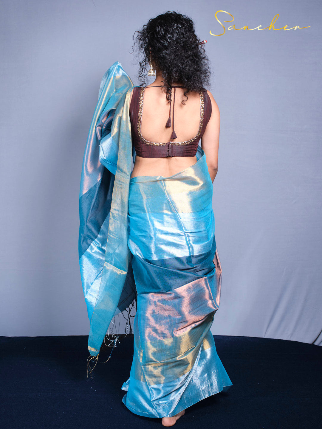Back pose of viewing the Elegant woman showcasing sea shine saree with curly hair.