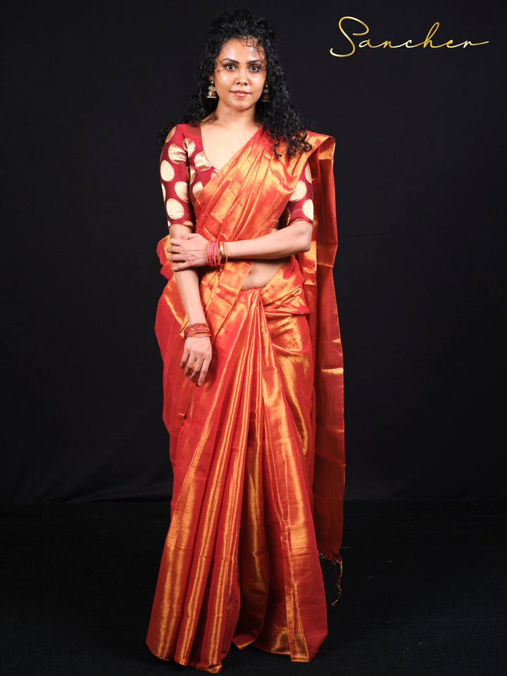 Woman wearing elegant sunset orange Mul Zari silk saree with golden border standing against black background