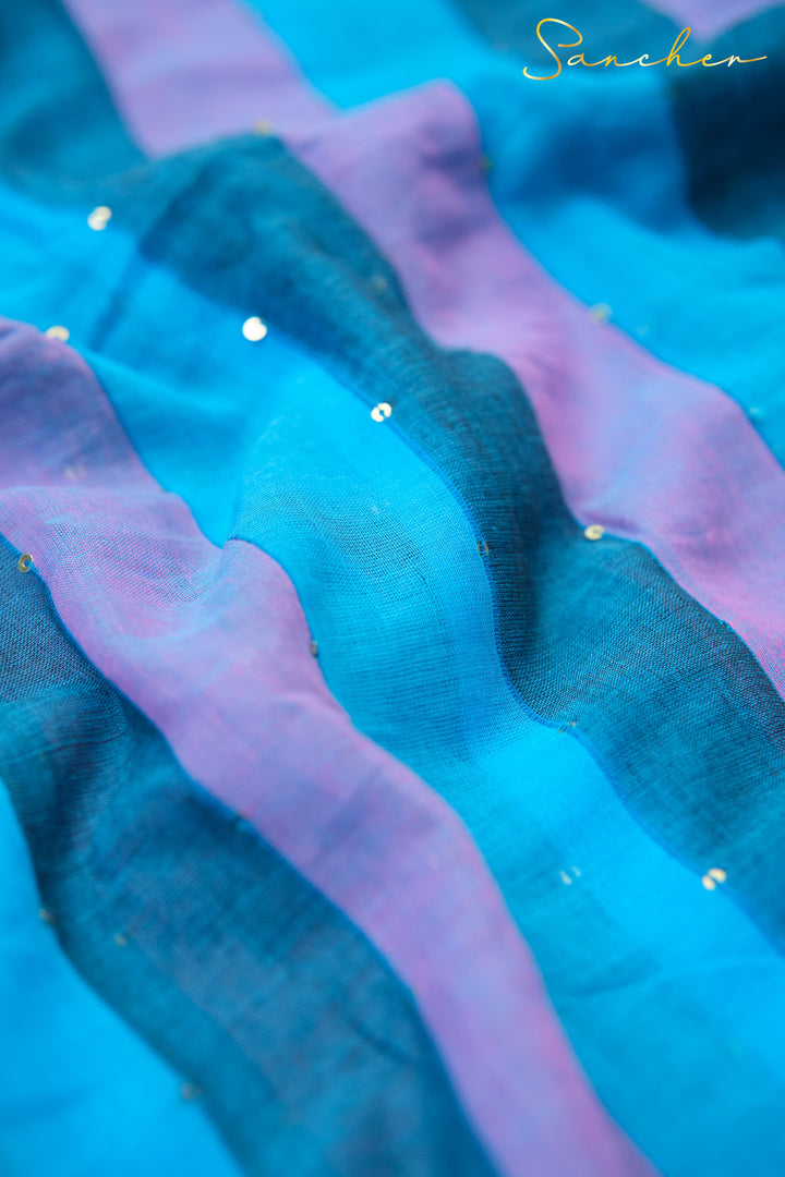 Close-up of blue and purple striped mulmul cotton saree fabric with subtle sheen and sequin embellishments. Elegant workwear saree texture from top saree boutique in Anna Nagar.