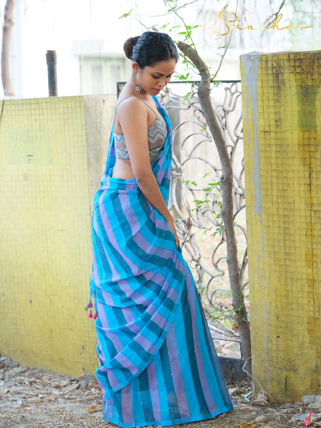 Side view of woman wearing blue and purple striped mulmul cotton saree, looking down. Ideal casual saree for office wear from best saree shops in Anna Nagar.
