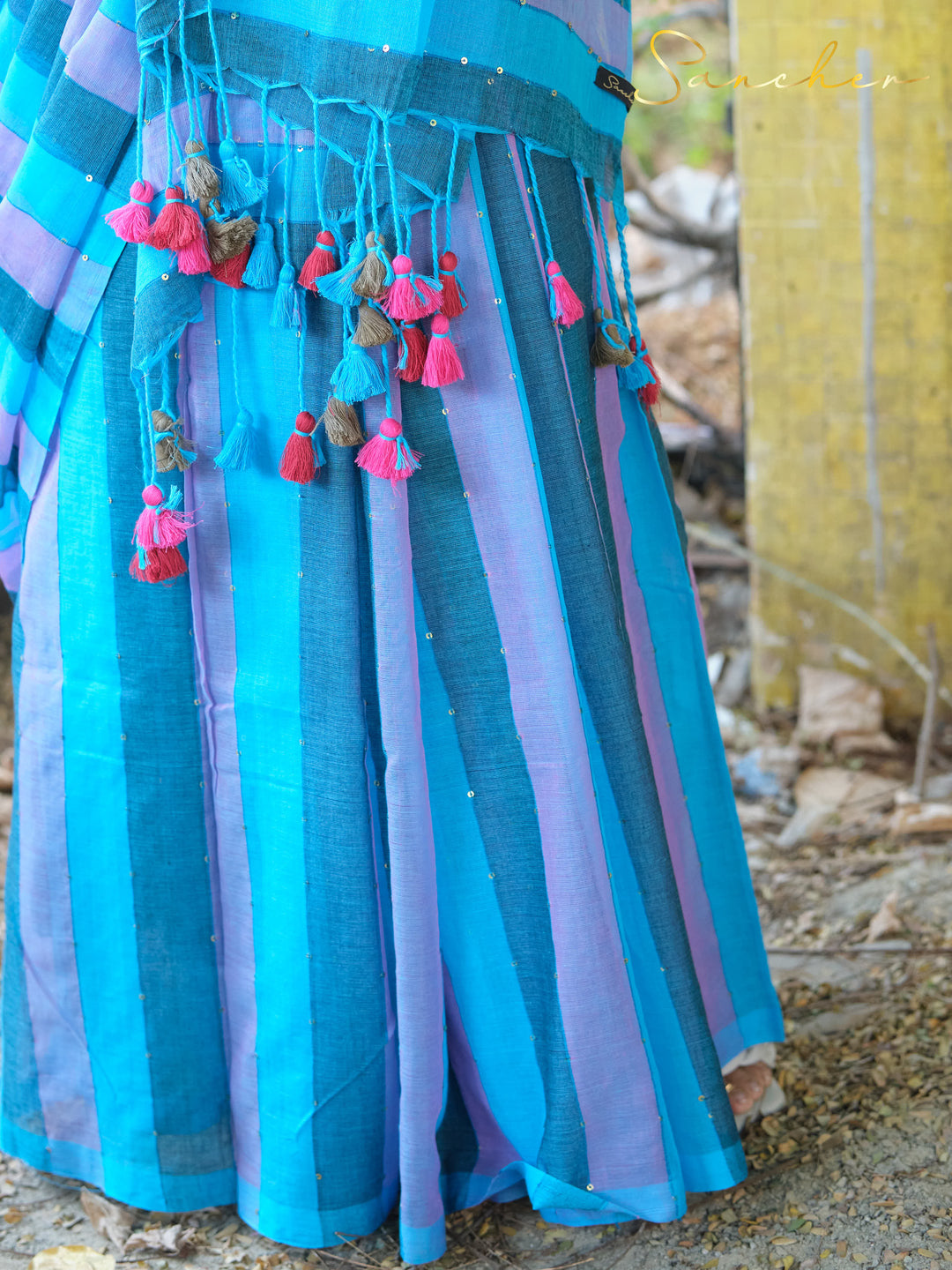 Bottom portion of blue and purple striped mulmul cotton saree with vibrant tassels in pink, blue, and beige. Versatile workwear saree from saree boutique in Anna Nagar.