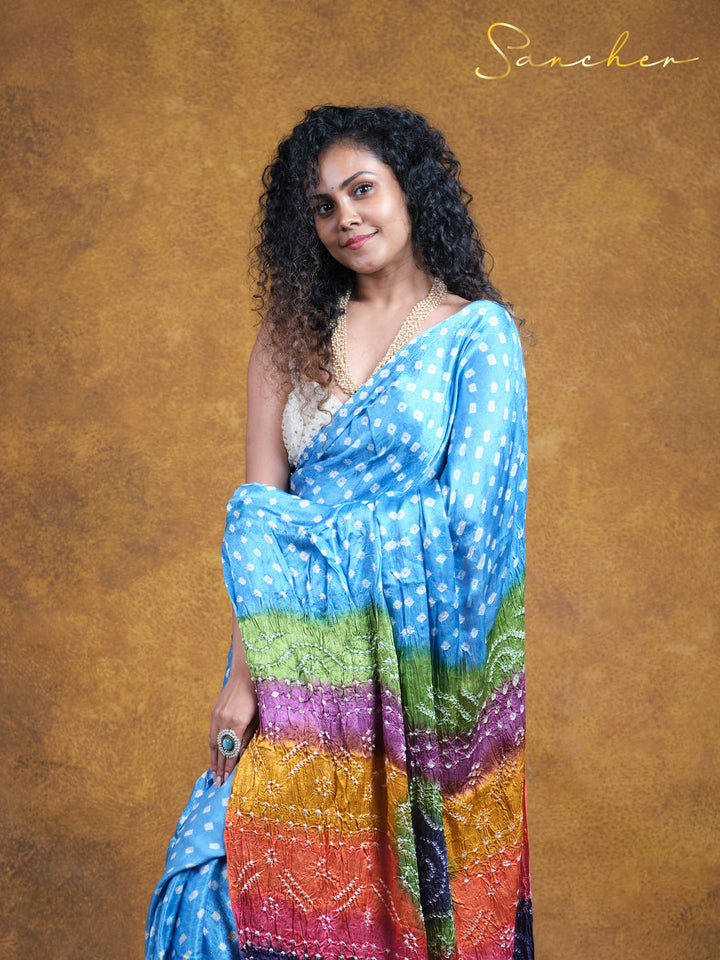 Modal silk Bandhani saree from Sancher, perfect for office wear. Light blue with white polka dots and vibrant rainbow pallu, ideal for professional workwear. Best saree shop in Anna Nagar for casual yet stylish office attire.