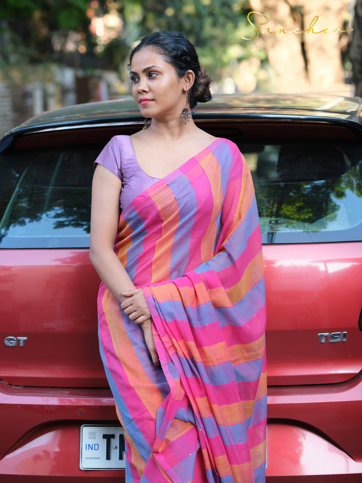 Smiling woman in colorful striped mulmul cotton saree and purple blouse, leaning against red car,Mul Cotton Sarees, Workwear sarees, Saree Boutique in Anna Nagar, Best Sarees Shops in Anna Nagar, Professional Office wear Sarees, Casual Sarees for Office Wear.