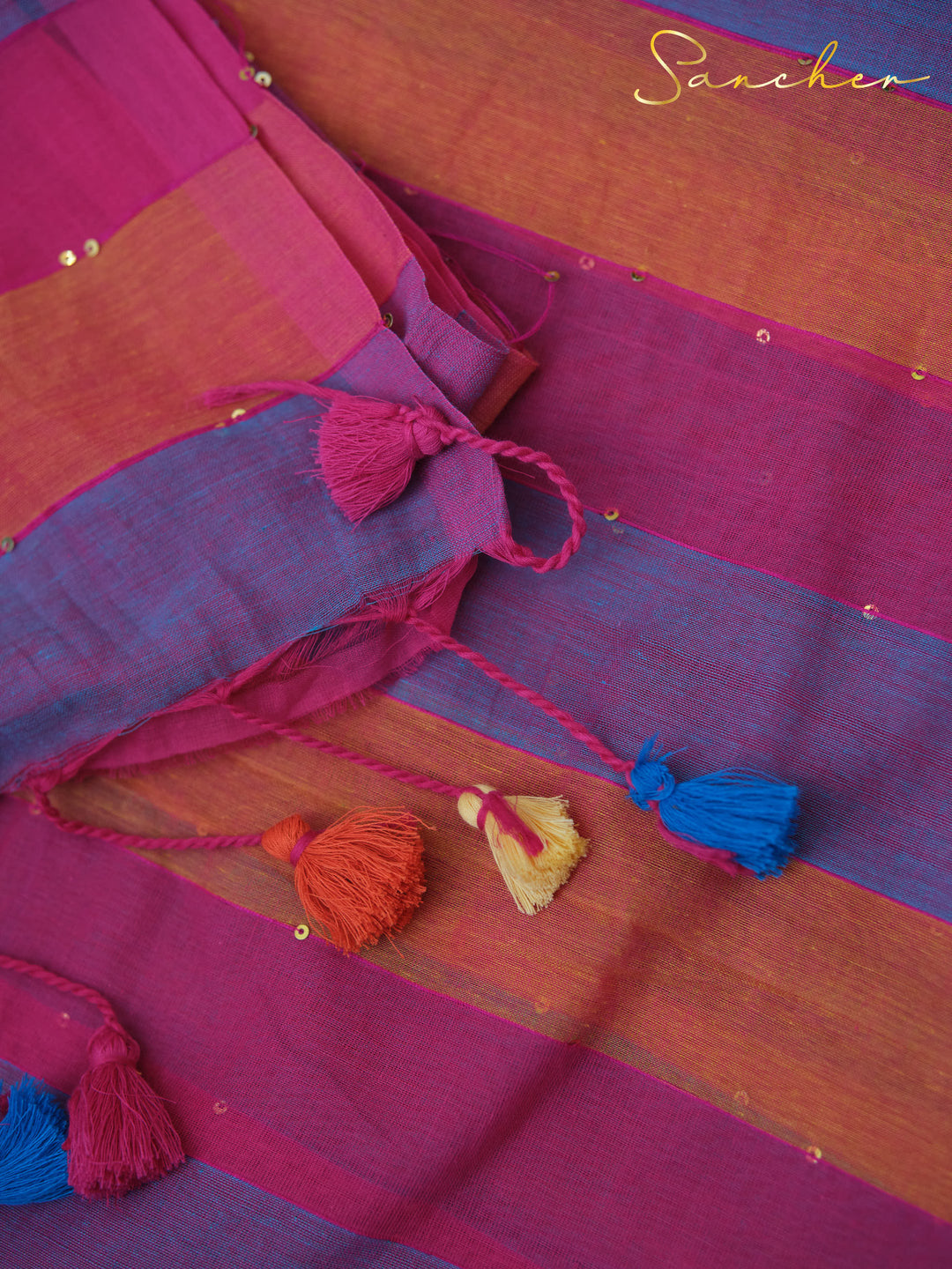 Colorful mulmul cotton fabric with stripes in pink, blue, and orange, adorned with small tassels in various colors and the "Sancher", Workwear sarees, Best Sarees Shops in Anna Nagar.