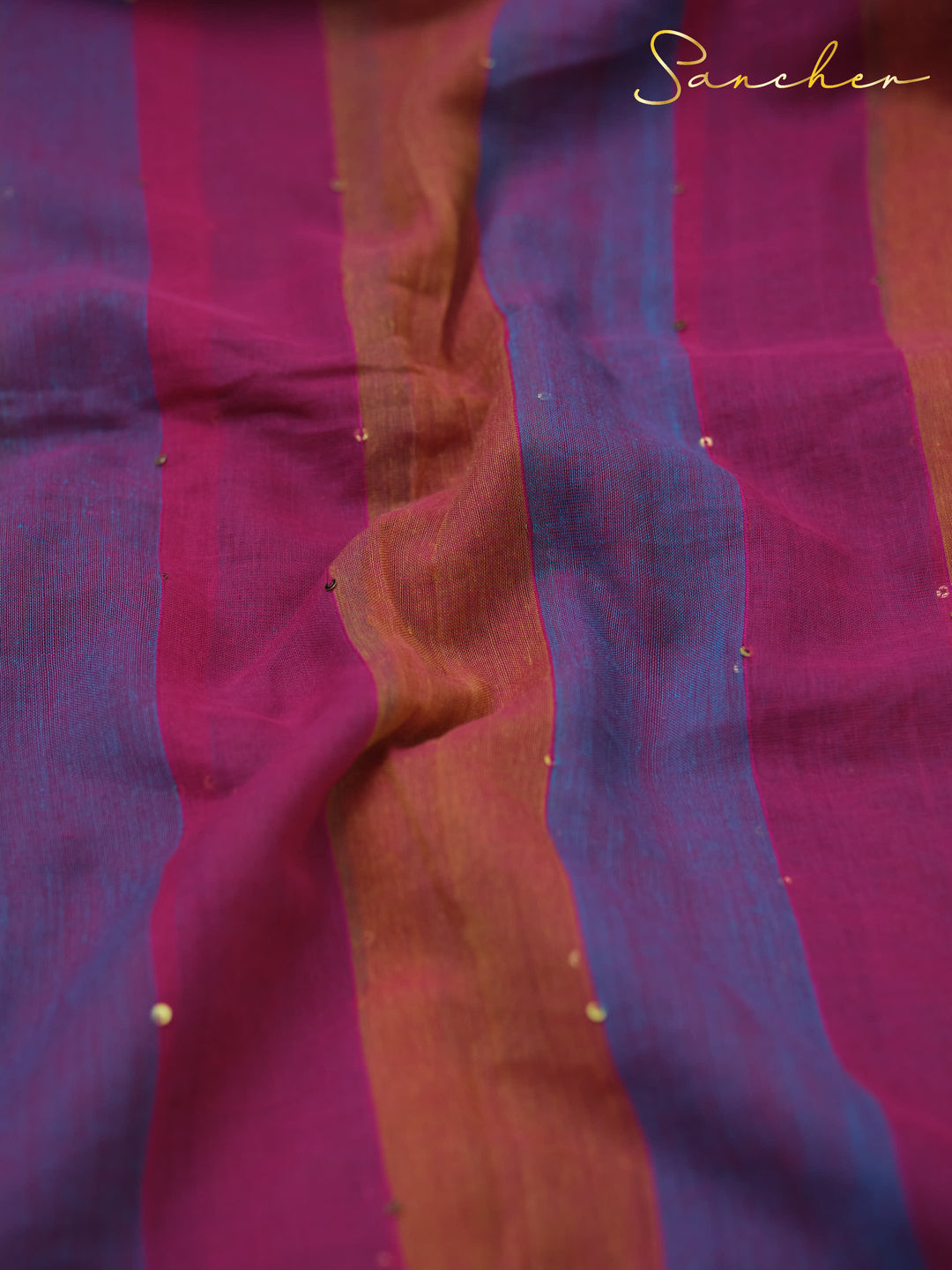 Close-up of vibrant striped mulmul cotton fabric in shades of purple, pink, and orange with subtle gold sequins, featuring the "Sancher", Mul Cotton Sarees, Saree Boutique in Anna Nagar.