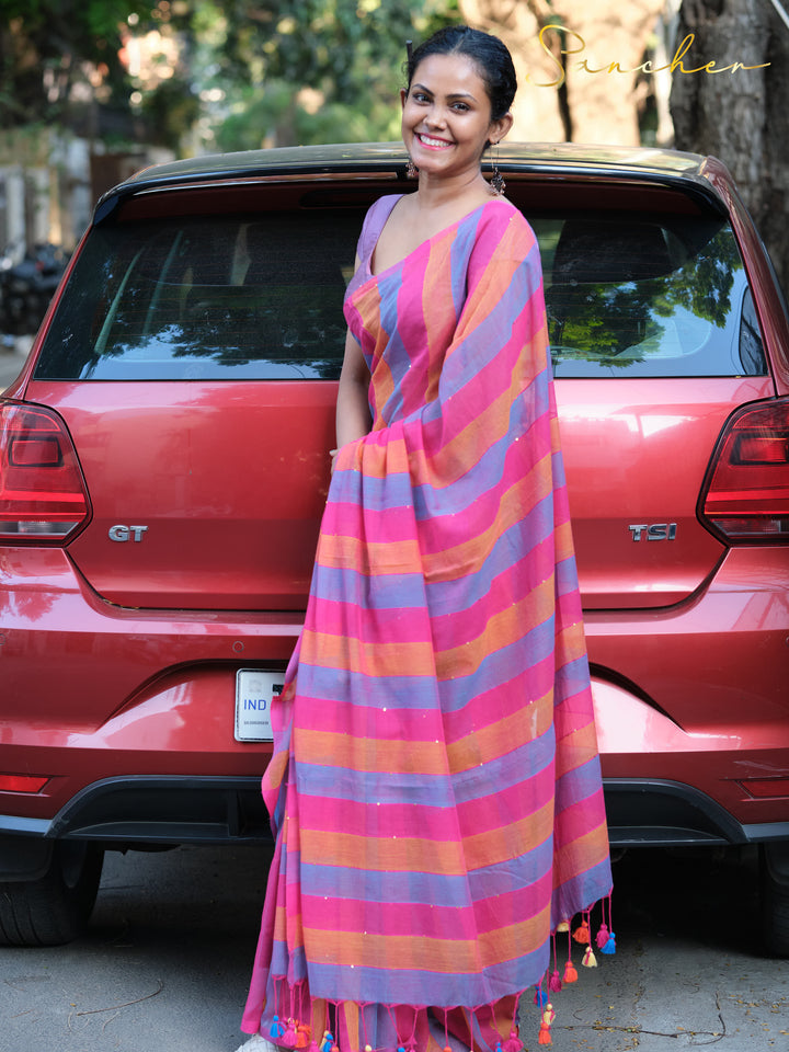 Woman in bright striped mulmul cotton saree and purple blouse, posing beside red car with "GT" badge, Mul Cotton Sarees, Workwear sarees, Saree Boutique in Anna Nagar, Best Sarees Shops in Anna Nagar, Professional Office wear Sarees, Casual Sarees for Office Wear.