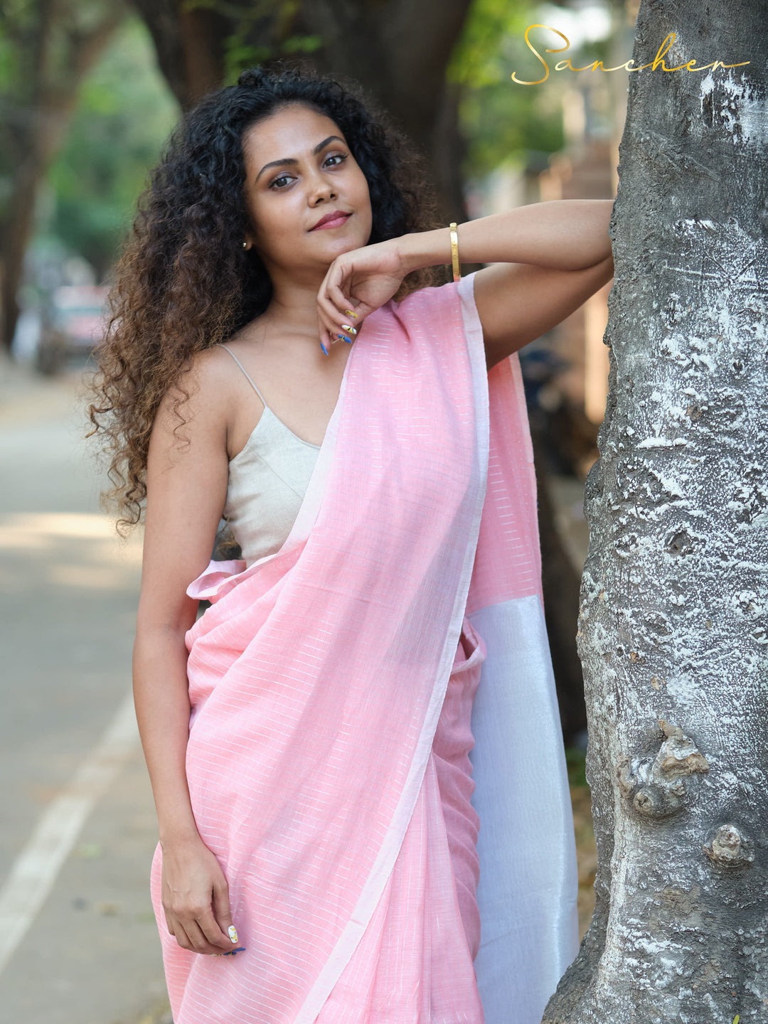 Woman in a pink and white mul cotton saree leaning against a tree, demonstrating the saree's comfort and style for professional settings. Keywords: Professional Office wear Sarees, Saree Boutique in Anna Nagar, Workwear sarees, Pink sarees Online